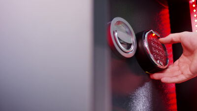 Hand tippt Code auf beleuchtetem Tresor Tastenfeld ein Hand tippt Code auf beleuchtetem Tresor Tastenfeld ein, beleuchtetes Tastenfeld, elektronisches Schloss und Zahlencode