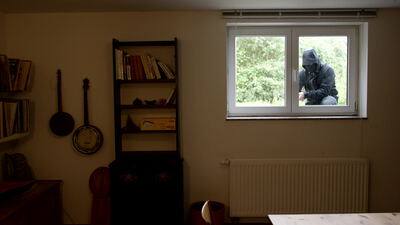 Maskierter Eindringling kauert am Fenster und greift von außen hinein
