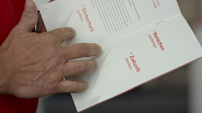 Hände blättern in einer aufgeklappten Firmenbroschüre im Büro
