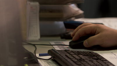 Bürokraft bedient die Computermaus am Schreibtisch mit Unterlagen