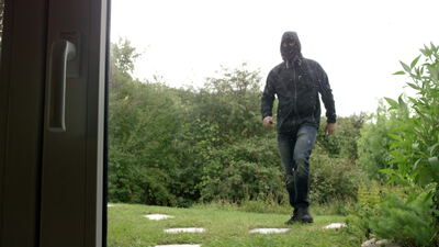 Maskierter Einbrecher nähert sich bei Regen einem Haus durch den Garten, Einbrecher im Garten, Einbruch Video und Einbrecher