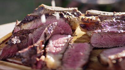 Grobes Salz fällt auf frisch gegrillte und aufgeschnittene Steaks auf einem Holzbrett