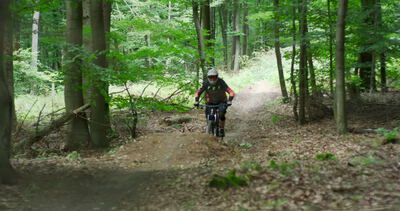 Downhill Mountainbiker rast über einen staubigen Waldweg