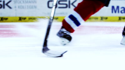 Eishockeyspieler führt Puck mit Schläger übers Eis