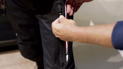 Hand öffnet den seitlichen Belüftungsreißverschluss einer schwarzen Motorradhose