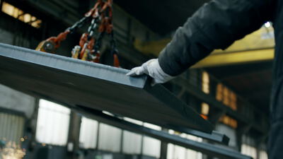 Arbeiter führt schweres Stahlblech am Kettenzug durch die Metallfabrik