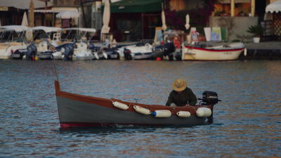 Mann mit Strohhut fährt in kleinem Holzboot durch den Hafen