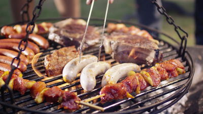 Bratwürste Steaks und Fleischspieße brutzeln auf einem Schwenkgrill über offenem Feuer