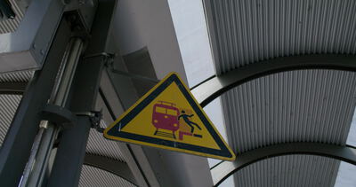 Gelbes Warnschild am Bahnsteig mit Zug Piktogramm in Nahaufnahme