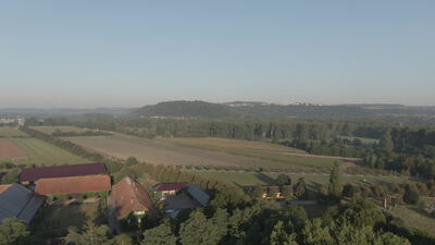 Drohne fliegt über Bauernhof und weite Felder im warmen Morgenlicht