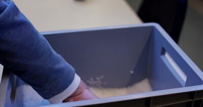 Hand hält eine blaue Kunststoffkiste mit Teilen in einer Fabrik