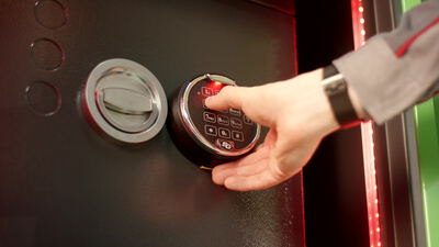 Hand gibt Zahlencode am elektronischen Tresorschloss ein und öffnet die Tür