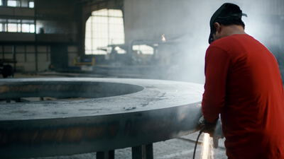 Arbeiter bearbeitet einen großen Stahlring in der Industriehalle