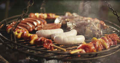 Würste, Spieße und Steaks garen auf einem rauchenden Schwenkgrill