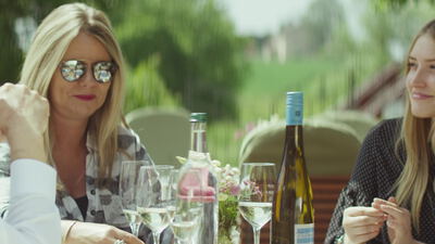 Zwei Freundinnen lachen bei einem Glas Weißwein im Sommergarten, blonde Frauen beim Wein, Freundinnen im Sommergarten und