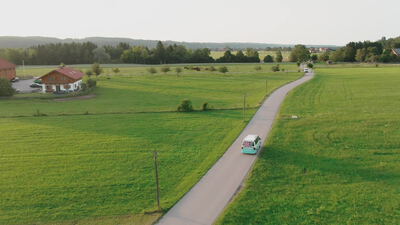 Türkiser Campingbus fährt über eine Landstraße im Abendlicht