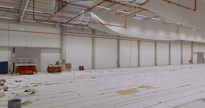 Hallenneubau mit orangen Scherenbühnen an der langen Wandseite