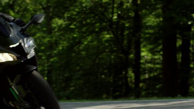 Motorrad fährt auf einer kurvigen Waldstraße durch grünen Wald, Sportmotorrad, Motorradfahrt und Landstraße als 4K Stockvideo