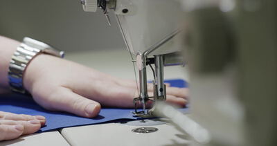 Näherin führt blauen Stoff an der Nähmaschine, Näherin näht blauen Stoff, Hände führen Stoff Nähmaschine und Nähmaschine