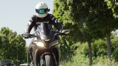 Motorradfahrer fährt auf einer Allee frontal auf die Kamera zu