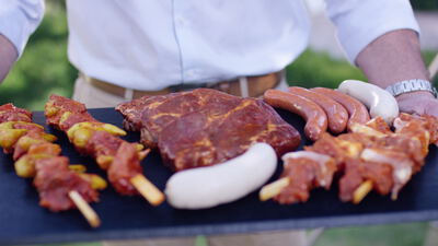 Ein Mann trägt eine Schieferplatte voller rohem Grillfleisch durch den Garten
