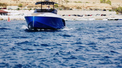 Blaues Motorboot fährt frontal über das offene Meer auf die Küste zu