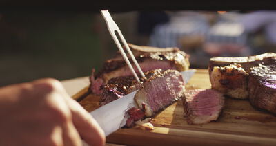 Gegrilltes Steak wird mit Messer und Fleischgabel auf einem Holzbrett tranchiert