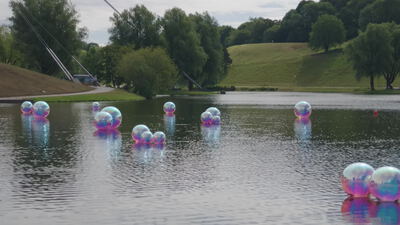 Kugeln schwimmen bunt schillernd auf einem ruhigen Parksee: Wasserkugeln, schwimmende Kunstinstallation
