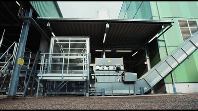 Industriemaschine mit Steigförderband vor einer grünen Werkshalle im Freien