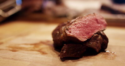 Kochmesser schneidet medium gebratenes Steak auf dem Holzbrett