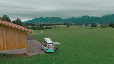 Drohnenaufnahme vom Campervan an einer Berghütte in der Alpenwiese