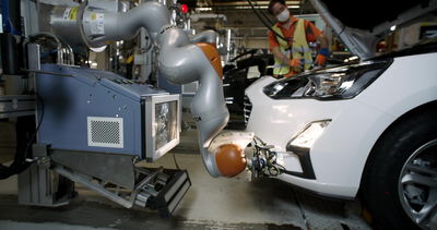 Roboterarm montiert die Front eines weißen Autos an der Fertigungslinie