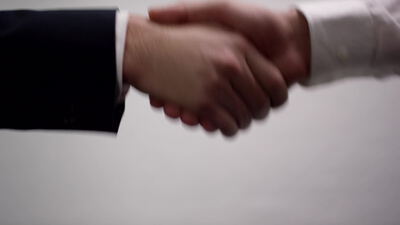 Handschlag zweier Geschäftsleute im Anzug vor grauem Hintergrund