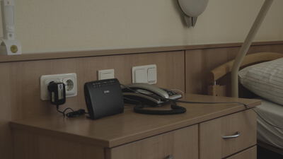 Nachttisch mit altem Telefon und Leselampe neben dem Bett in einem schlichten Zimmer