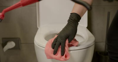 Reinigungskraft wischt Toilettensitz mit rosa Mikrofasertuch ab