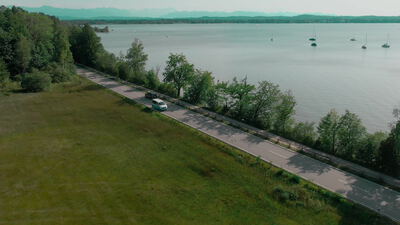 Drohnenaufnahme einer Seeuferstraße an einem großen See mit Segelbooten
