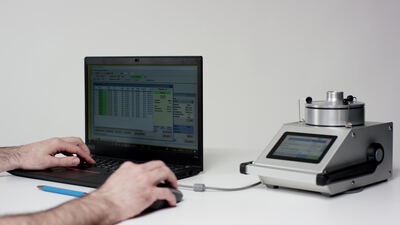 Hände bedienen Laptop neben Messgerät bei der Qualitätsprüfung