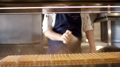 Kakaopulver rieselt über kleine Pralinen hinter Glas Kakaopulver rieselt über kleine Pralinen hinter Glas, Kakaopulver bestäuben, kleine Pralinen in Reihen und Streuer in der
