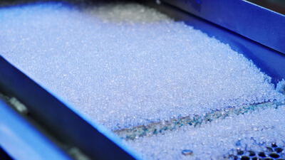 Breites Bett aus Kunststoffgranulat auf einer blauen Siebmaschine, Sortieranlage, Kunststoffpellets und Granulatbett als 4K