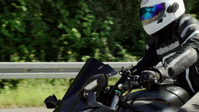 Motorradfahrer auf einem Sportmotorrad fährt an einer Leitplanke entlang, Lederkombi, Integralhelm und Motorradhelm als 4K