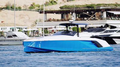 Blaues Sportboot gleitet vor einem Jachthafen über ruhiges Wasser