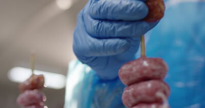 Fleischspieße werden mit blauen Handschuhen in der Produktion gehalten