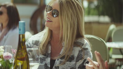 Blonde Frau unterhält sich angeregt am Tisch im Freien, Frau im Gespräch, blonde Frau Sommer und angeregtes Gespräch als 4K