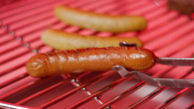 Gegrillte Bratwürste auf einem roten Grillrost werden gewendet
