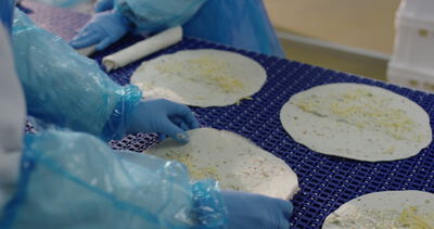 Mitarbeiter belegen Teigfladen mit Käse auf dem blauen Förderband