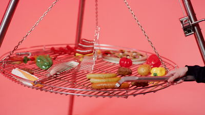 Schwenkgrill mit Bratwurst und Gemüse vor rosa Hintergrund
