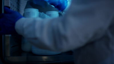 Laborkraft mit blauen Handschuhen nimmt weiße Behälter aus dem Regal