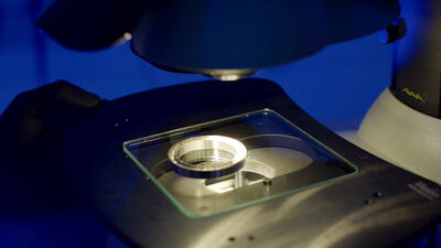 Labormikroskop untersucht eine runde Metallprobe im blauen Licht