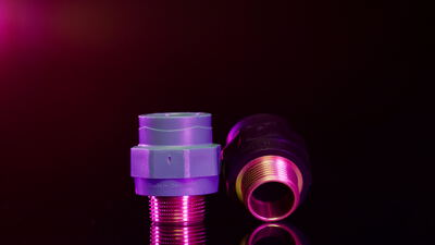 Zwei Rohrverbinder liegen dicht beieinander im violetten Studiolicht