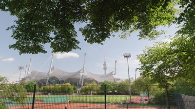 Eingezäunte Tennisplätze liegen unter Flutlichtmasten vor einem Fernsehturm: Tennisplatz, eingezaeunter Tennisplatz